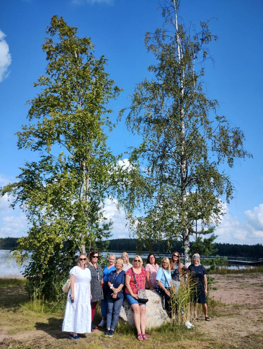 Projektitiimi poseeraa koivujen edessä, taustalla joki.